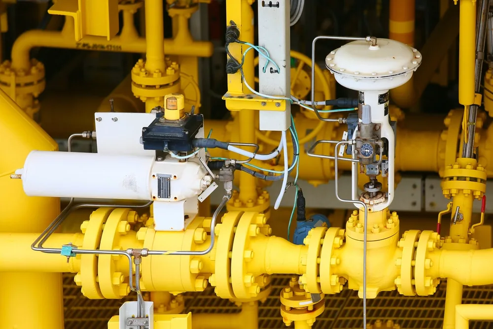 Control valve with a pneumatic actuator and positioner installed on yellow pipework at a gas facility.