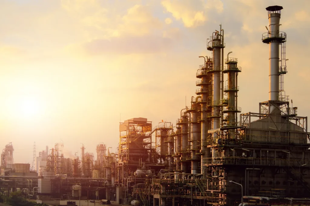 Refinery silhouetted against a golden sunrise, with a worker walking in the foreground.