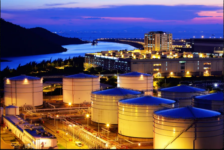 Tank terminal at dusk, with rows of storage tanks lit along a waterfront.