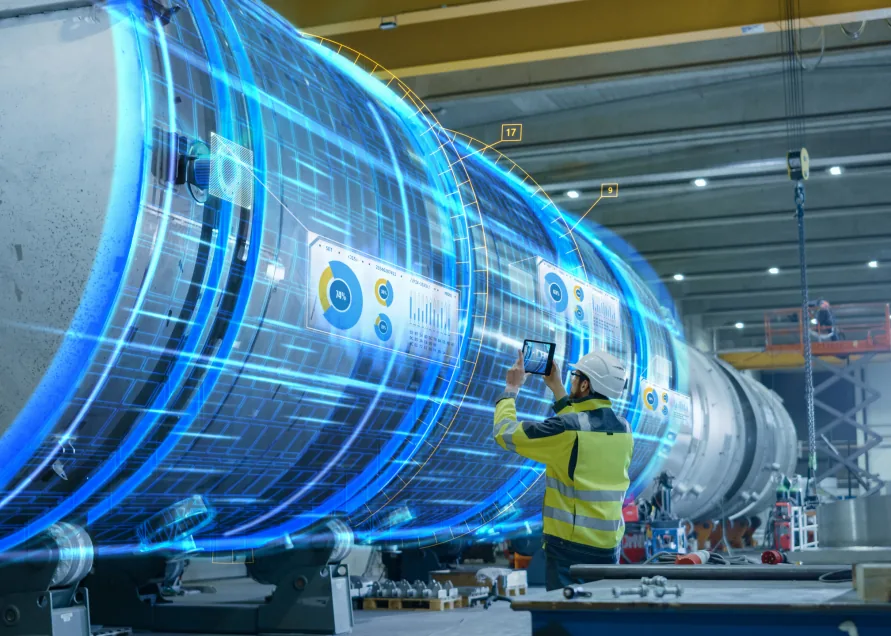 Engineer photographing a large industrial vessel with a tablet, overlaid with a glowing blue digital twin wireframe of the same vessel.