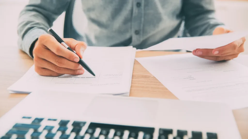 Person at a desk writing calculations on printed spreadsheets.