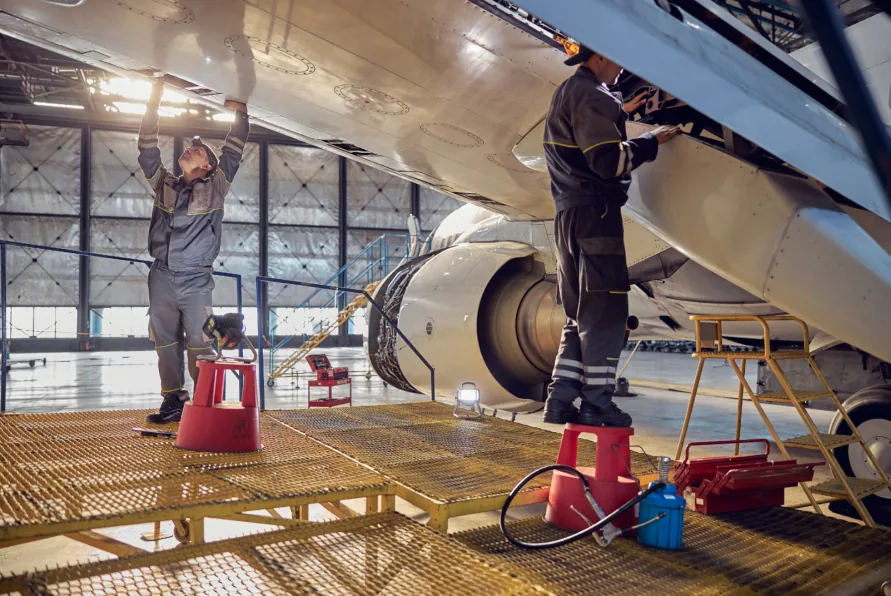 Aircraft maintenance in a hangar, with engineers on platforms working beneath the fuselage and engine.
