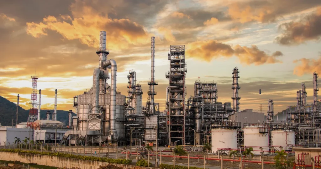 Refinery at sunset, with distillation columns, flare stacks and storage tanks under a dramatic sky.