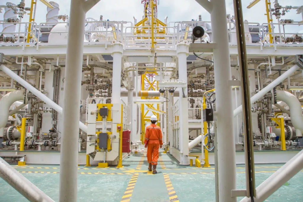 Worker in orange coveralls walking along a walkway between process modules on an offshore platform.