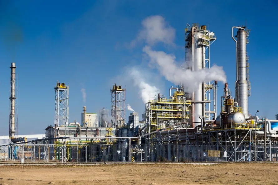 Chemical plant with distillation columns and stacks emitting steam, under a blue sky.