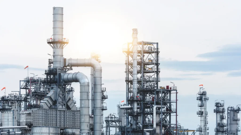 Refinery with distillation columns and pipework, lit by low sun.