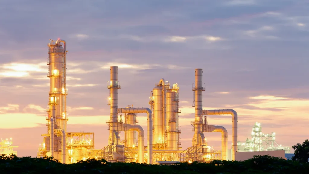 Refinery lit at dusk, with distillation columns and stacks against a coloured sky.