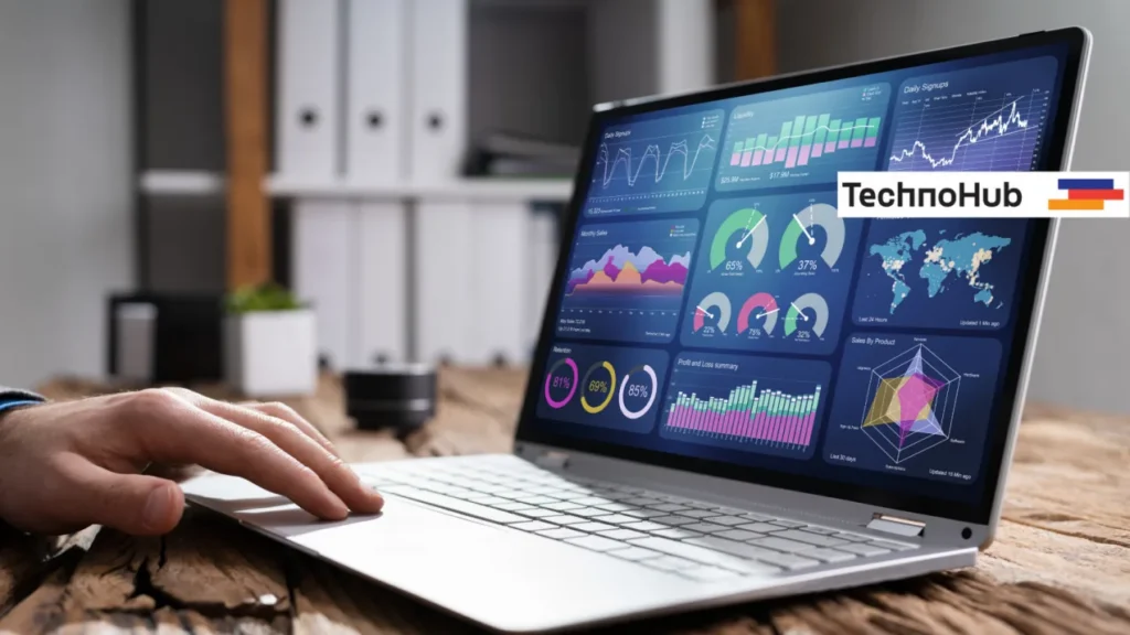 Hand using a laptop that displays an analytics dashboard of charts, gauges and a world map, with the TechnoHub logo alongside.