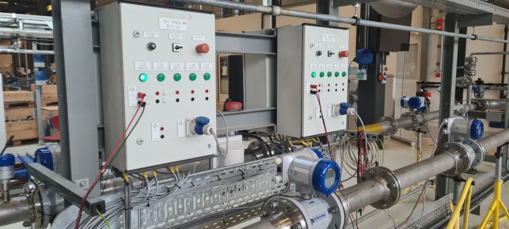 Pilot plant skid with stainless steel pipework, flow instrumentation and two control cabinets.