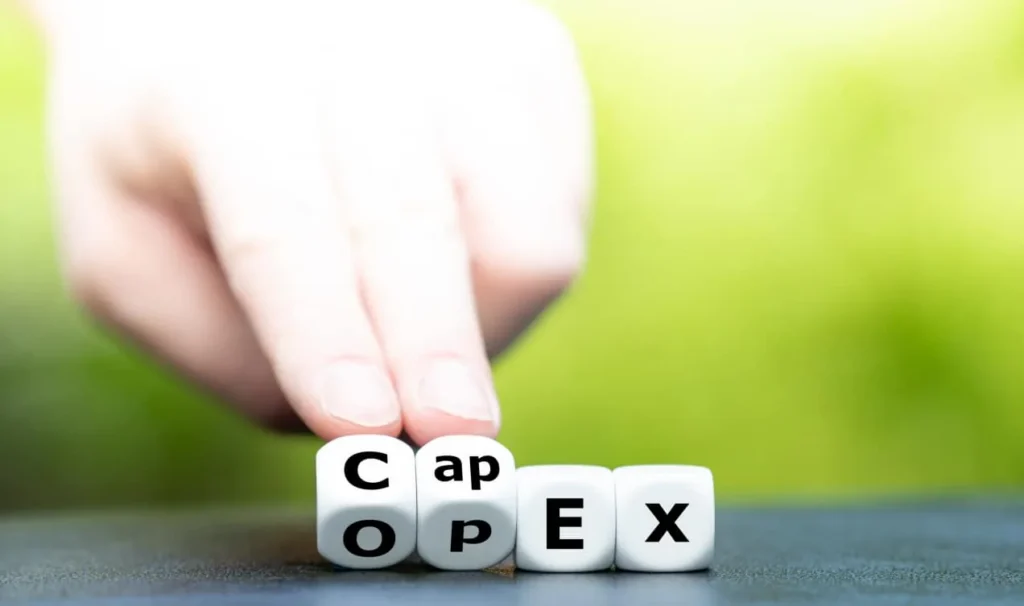 Hand turning a lettered dice so that the word OPEX changes to CAPEX.