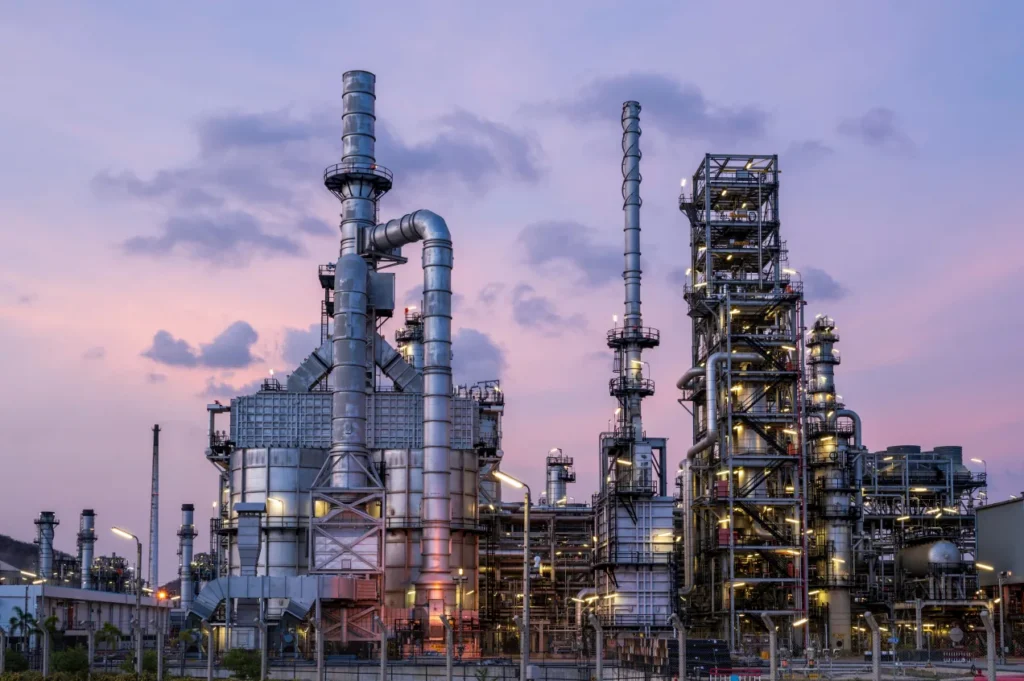 Refinery at dusk, its columns and stacks lit against a purple sky.