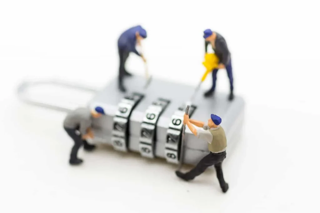 Miniature figurines of workers climbing over a combination padlock and turning its dials.