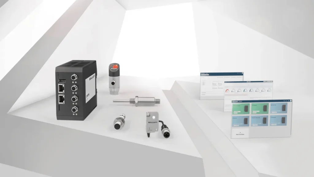 Balluff condition monitoring hardware, an industrial gateway, sensors and connectors, displayed beside dashboard screens on a white background.