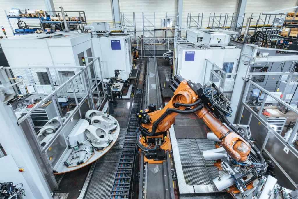 Overhead view of an automated production cell with orange robotic arms handling components on a conveyor.