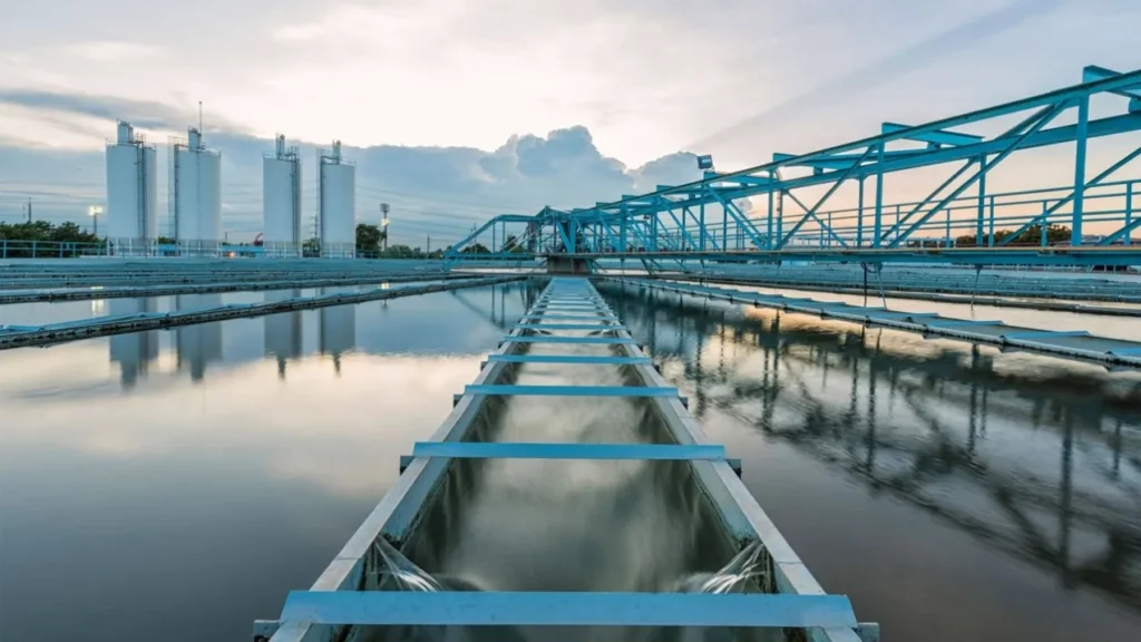 Long rectangular sedimentation basins at a water treatment works, reflecting the sky, with walkways running the length of the tanks.