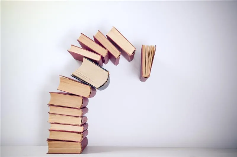 Stack of old hardback books curving upward with volumes balanced along its top edge, one standing open at the end.