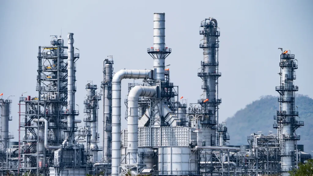 Petrochemical plant with distillation columns and pipework, with hills behind.