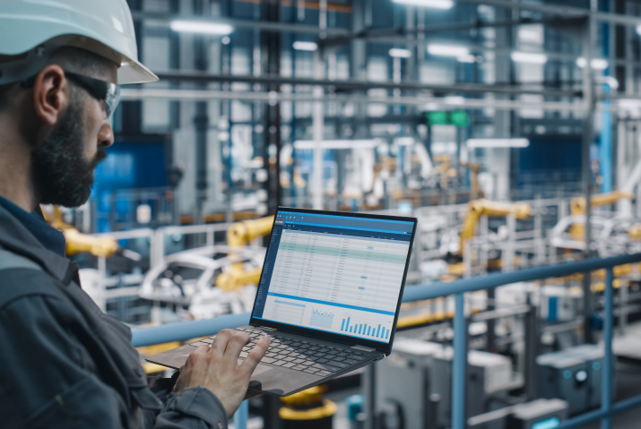 Car Factory Engineer in Work Uniform Using Laptop Computer with Spreadsheet Software